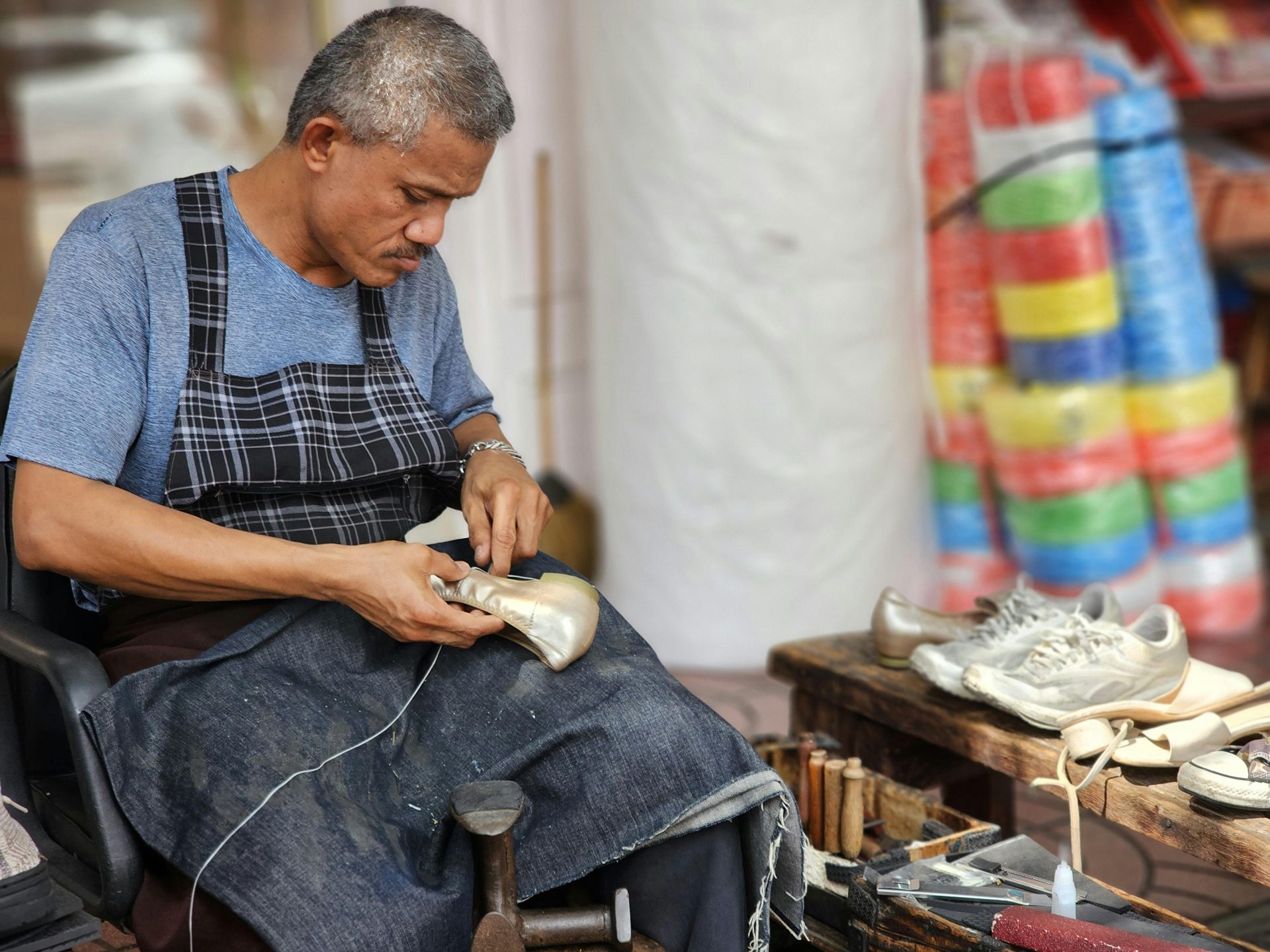 Artisan shoemaker working on shoes in his workshop with tools and materials around.