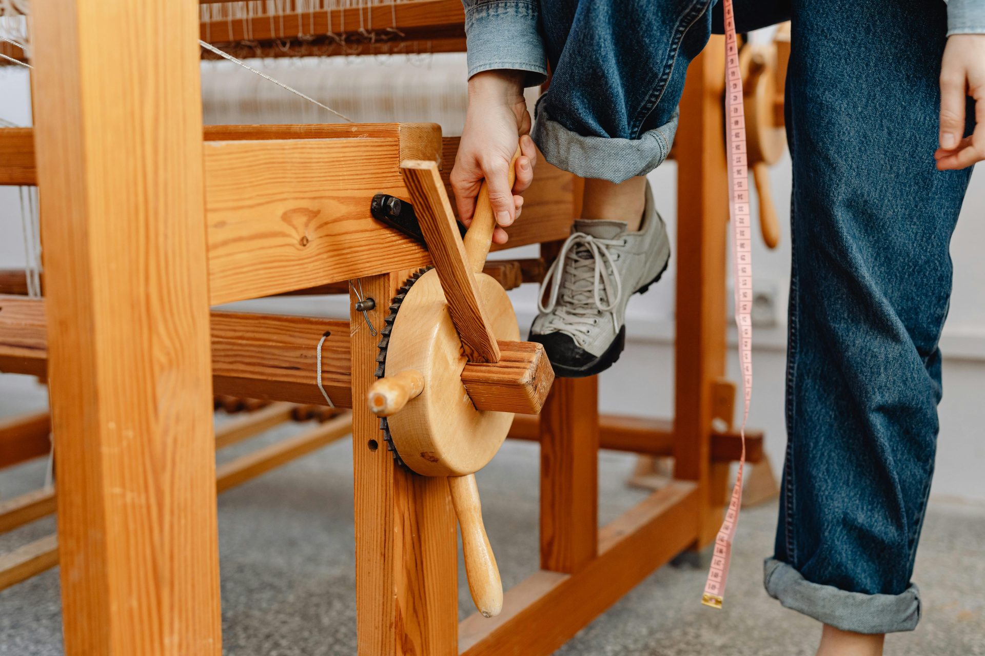 A person using a wooden weaving loom, showing detail of hand and machinery.